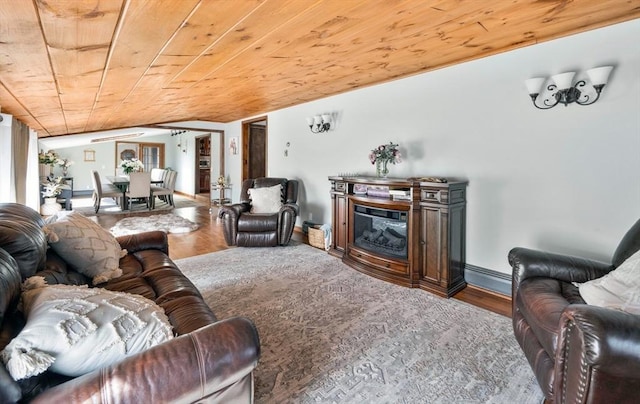 living room featuring a glass covered fireplace, wooden ceiling, baseboards, and wood finished floors