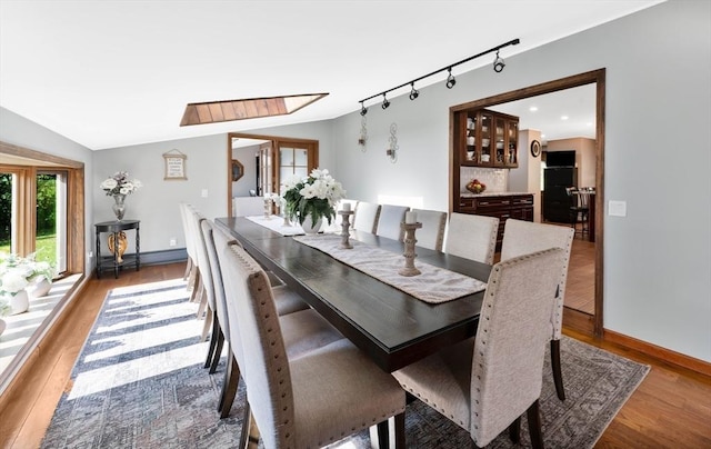 dining space featuring baseboards, rail lighting, lofted ceiling with skylight, and wood finished floors