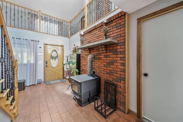 entrance foyer with baseboards, a high ceiling, a wood stove, and wood finished floors