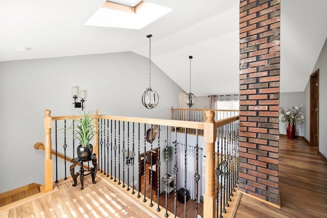 corridor featuring wood finished floors, baseboards, a chandelier, vaulted ceiling with skylight, and an upstairs landing