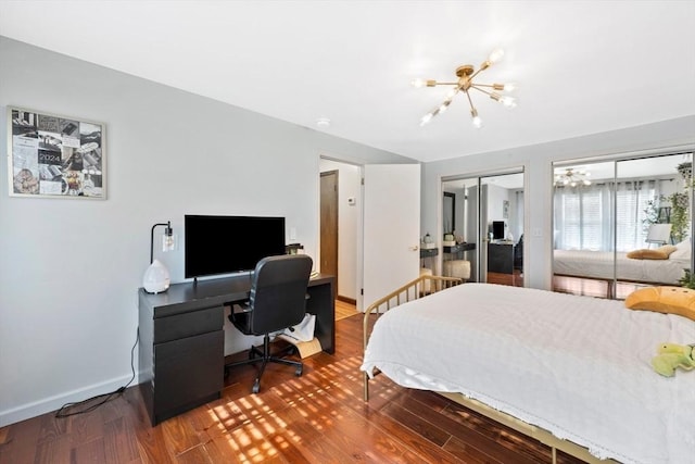 bedroom featuring two closets, baseboards, a notable chandelier, and wood finished floors