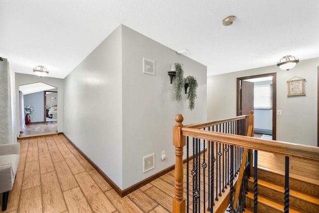 hallway with baseboards, visible vents, light wood-type flooring, and an upstairs landing