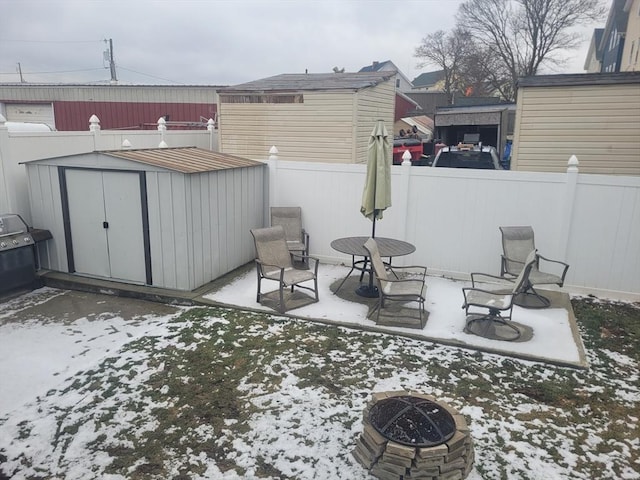 snow covered patio with a shed and an outdoor fire pit