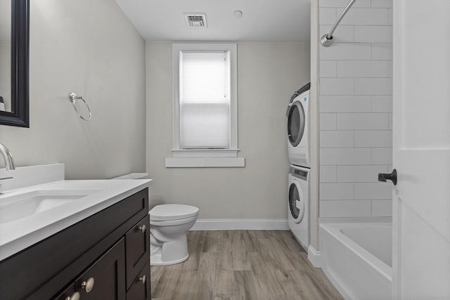 full bathroom featuring bathing tub / shower combination, stacked washer / drying machine, toilet, vanity, and hardwood / wood-style flooring