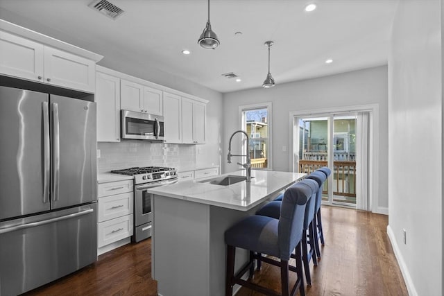 kitchen with white cabinets, sink, an island with sink, decorative light fixtures, and stainless steel appliances