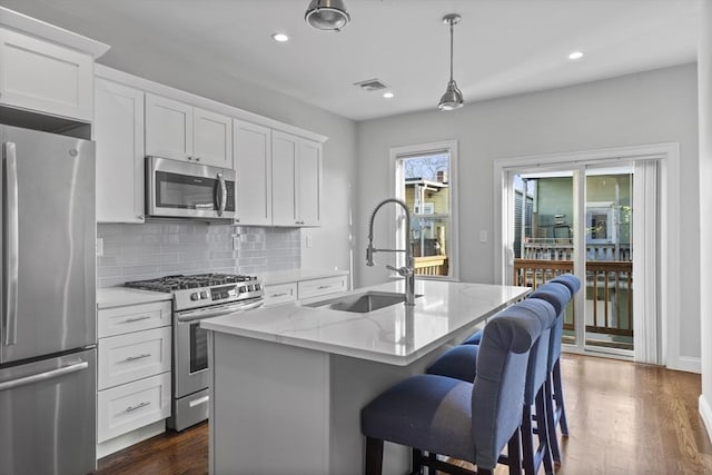 kitchen with stainless steel appliances, light stone counters, white cabinetry, and sink