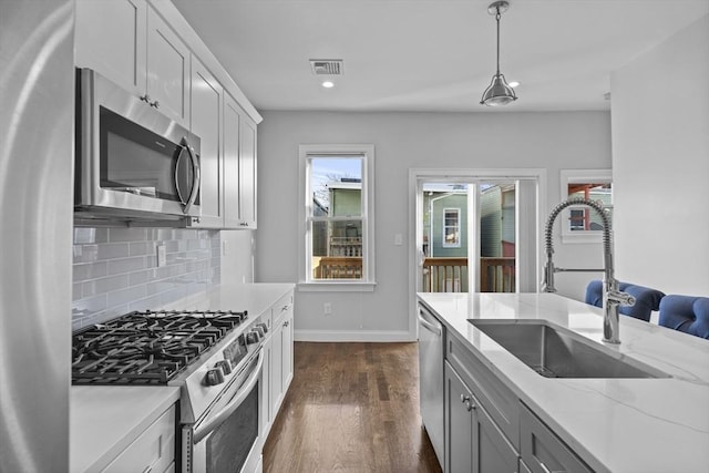 kitchen with tasteful backsplash, stainless steel appliances, sink, pendant lighting, and white cabinetry