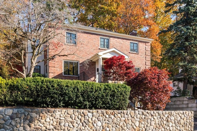 colonial inspired home with brick siding and a chimney