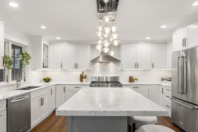 kitchen featuring a kitchen island, white cabinets, stainless steel appliances, wall chimney exhaust hood, and a sink