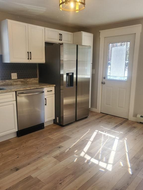 kitchen with white cabinets, light wood finished floors, stainless steel appliances, and backsplash