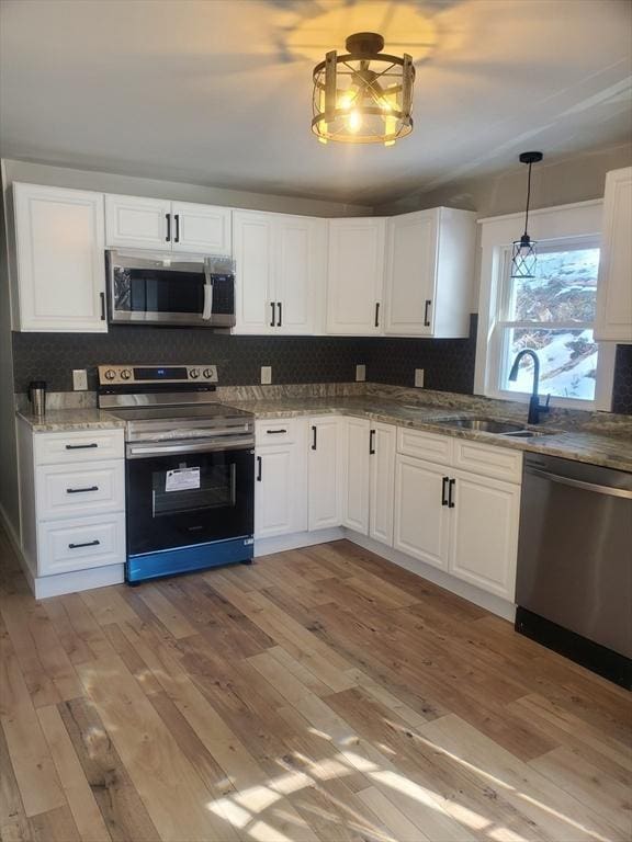 kitchen with stainless steel appliances, a sink, light wood-style flooring, and decorative backsplash