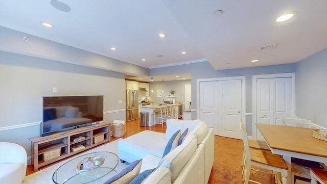 living room featuring crown molding, recessed lighting, visible vents, and light wood-type flooring