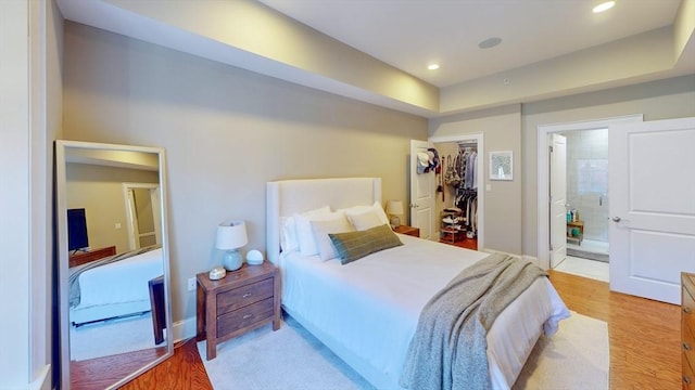 bedroom with a closet, ensuite bathroom, recessed lighting, a spacious closet, and light wood finished floors