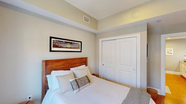 bedroom with baseboards, a closet, wood finished floors, and visible vents