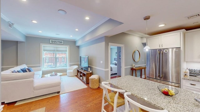 kitchen featuring crown molding, freestanding refrigerator, visible vents, white cabinetry, and light stone counters