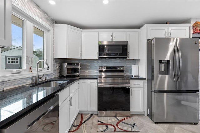 kitchen featuring light parquet floors, sink, dark stone countertops, appliances with stainless steel finishes, and white cabinetry