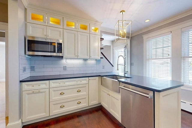 kitchen featuring dark wood-style floors, stainless steel appliances, ornamental molding, a sink, and a peninsula