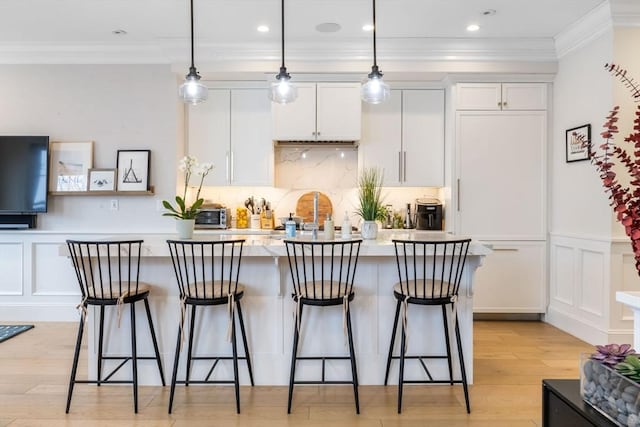 kitchen with a center island with sink, white cabinetry, hanging light fixtures, and light hardwood / wood-style flooring