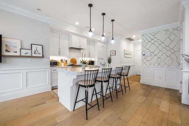 kitchen with a breakfast bar, light hardwood / wood-style floors, white cabinetry, hanging light fixtures, and an island with sink