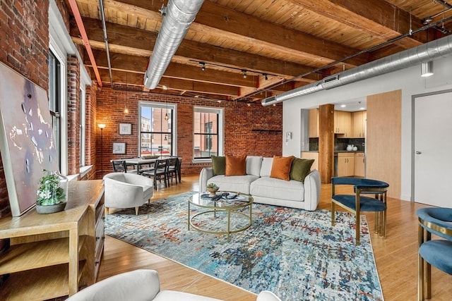 living room featuring track lighting, beamed ceiling, brick wall, and wood finished floors