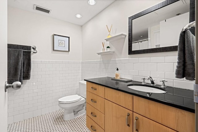 full bathroom with tile walls, visible vents, toilet, vanity, and tile patterned floors