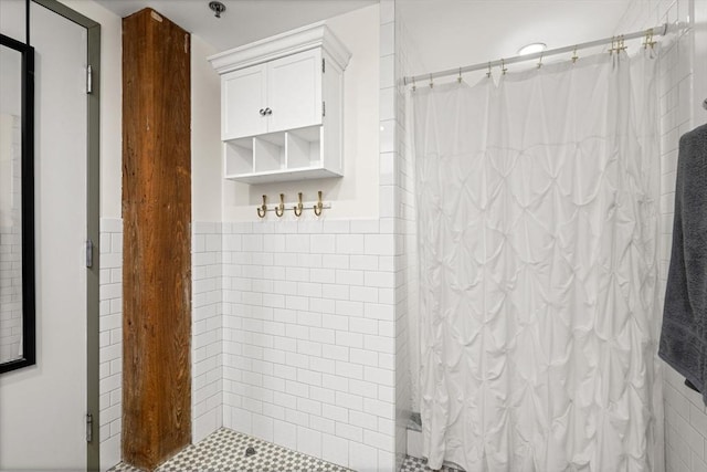 full bathroom with a wainscoted wall, a tile shower, and tile walls