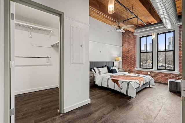 bedroom featuring brick wall, wood finished floors, beam ceiling, and baseboards