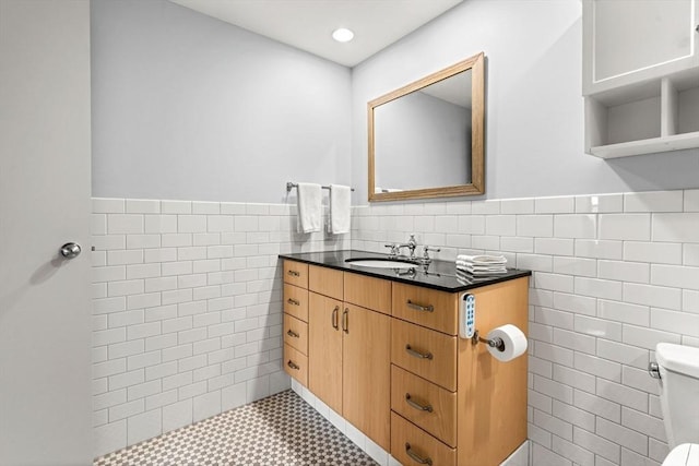 bathroom featuring toilet, a wainscoted wall, vanity, and tile walls