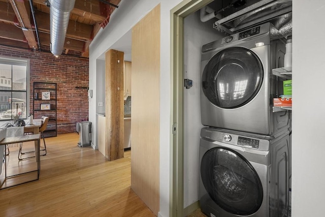 laundry area featuring stacked washer and dryer, brick wall, and light wood-style floors