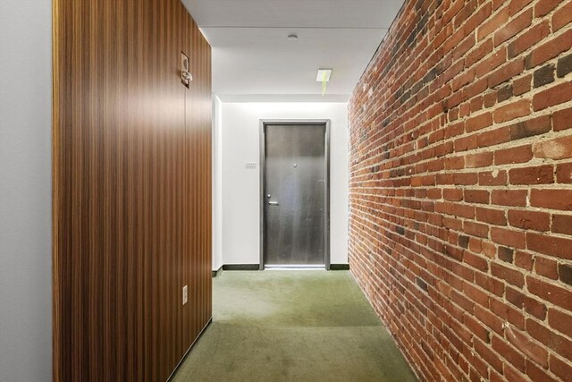 hallway with carpet, baseboards, and brick wall