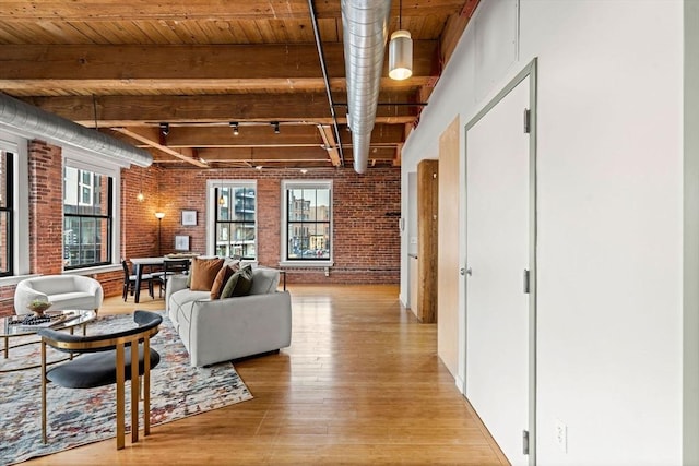 living area with a wealth of natural light, brick wall, light wood-style flooring, and beam ceiling