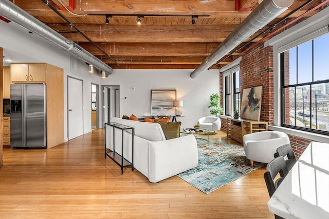 living room featuring brick wall, a high ceiling, light wood-type flooring, beam ceiling, and rail lighting