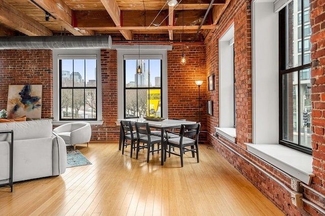 dining area with brick wall, light wood finished floors, and beam ceiling