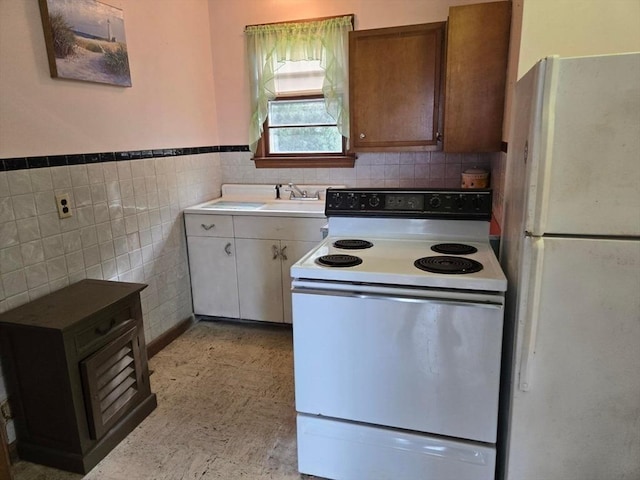 kitchen with light floors, white appliances, tile walls, a wainscoted wall, and a sink