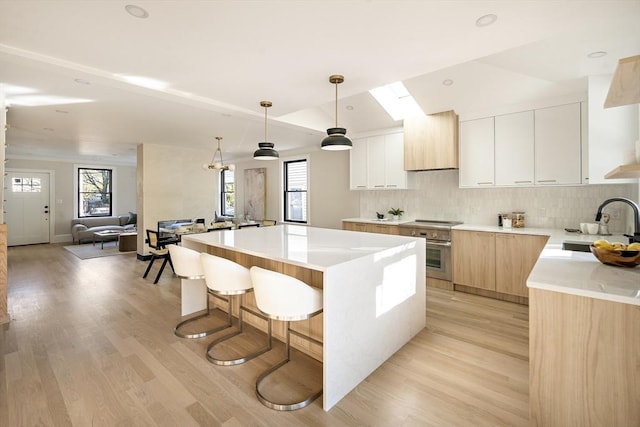 133 Fayerweather St Unit 1, Cambridge, MA 02138 - kitchen with wall oven, modern cabinets, a center island, light wood-type flooring, and backsplash