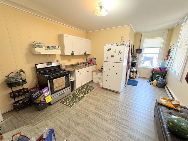 kitchen featuring freestanding refrigerator, light wood-style floors, stainless steel gas range oven, under cabinet range hood, and white cabinets