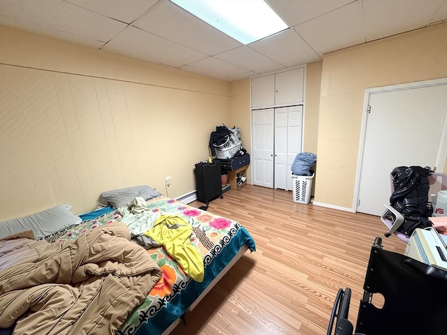 bedroom featuring light wood finished floors, a paneled ceiling, baseboards, a baseboard heating unit, and a closet