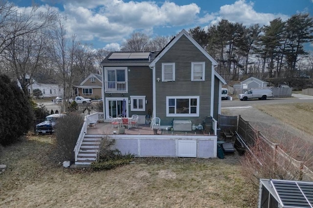 back of property with solar panels, a wooden deck, and a yard