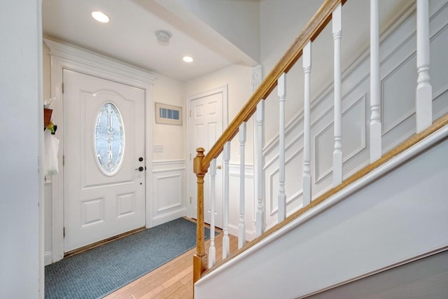 foyer entrance featuring stairs, wainscoting, recessed lighting, wood finished floors, and a decorative wall