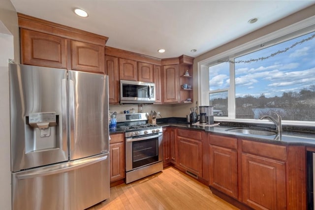 kitchen featuring dark stone countertops, a sink, light wood-style floors, appliances with stainless steel finishes, and brown cabinets