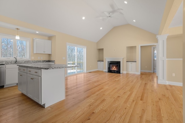 kitchen featuring hanging light fixtures, a center island, light wood-type flooring, stone counters, and ceiling fan