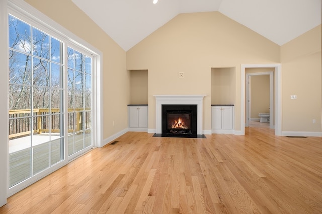 unfurnished living room with high vaulted ceiling, a healthy amount of sunlight, and light wood-type flooring