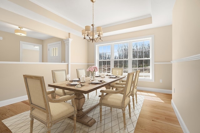 dining area with a tray ceiling, ornamental molding, light hardwood / wood-style flooring, and a chandelier