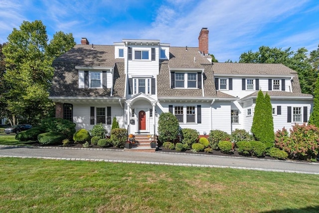 view of front of home with a shingled roof, a chimney, and a front yard