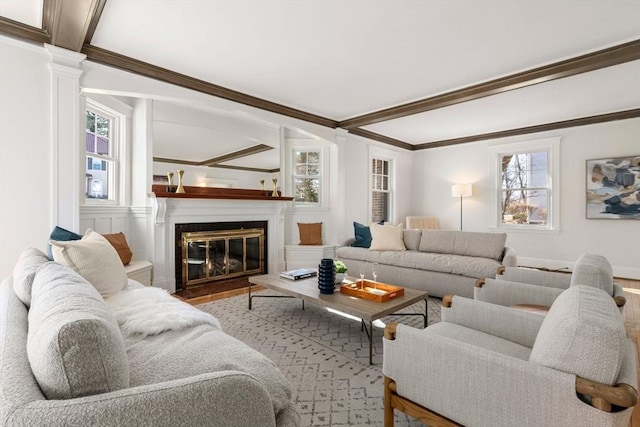 living room with wood finished floors, a fireplace with flush hearth, decorative columns, and crown molding