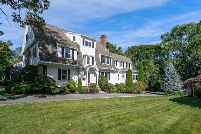 shingle-style home with a shingled roof, a front yard, a chimney, and a gambrel roof