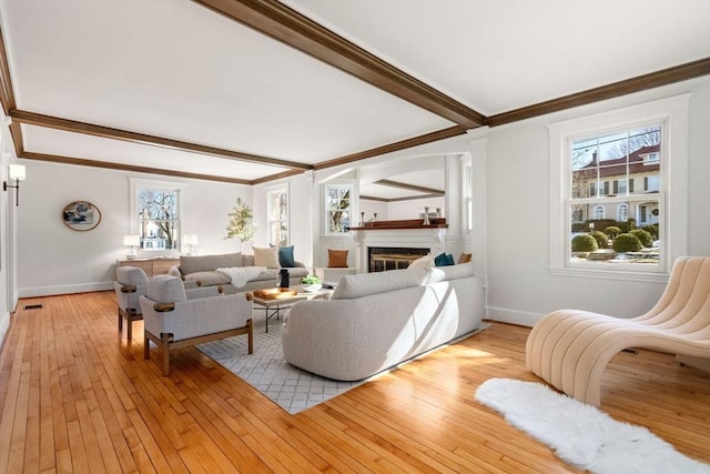 living room with a glass covered fireplace, beam ceiling, a healthy amount of sunlight, and light wood finished floors