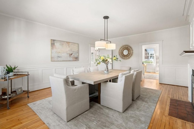 dining area featuring a fireplace with flush hearth, ornamental molding, and light wood finished floors