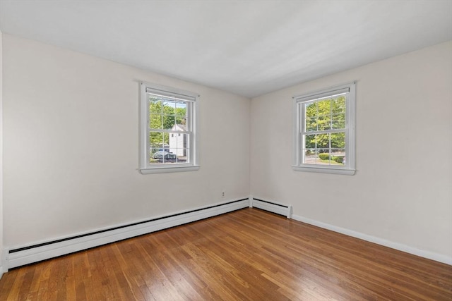 empty room with baseboard heating, wood finished floors, and baseboards