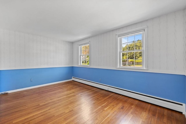 empty room with baseboard heating, wood finished floors, and baseboards